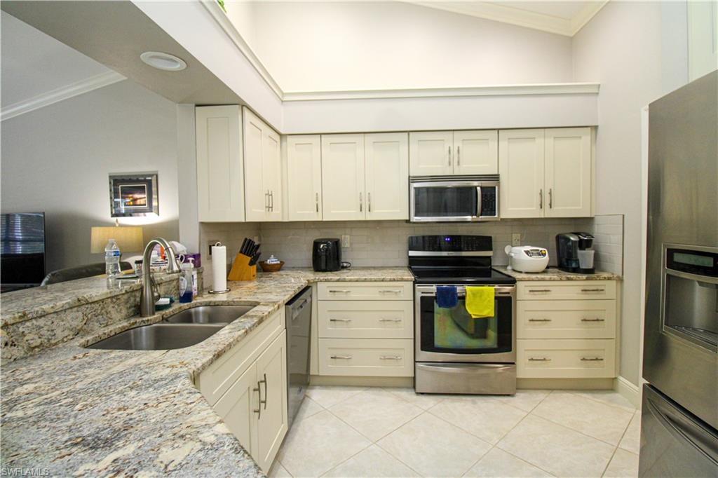 Kitchen with a sink, light stone counters, appliances with stainless steel finishes, crown molding, and light tile patterned floors