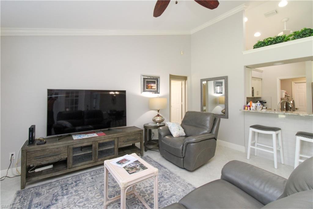 Living room featuring ornamental molding, a high ceiling, light tile patterned floors, baseboards, and ceiling fan