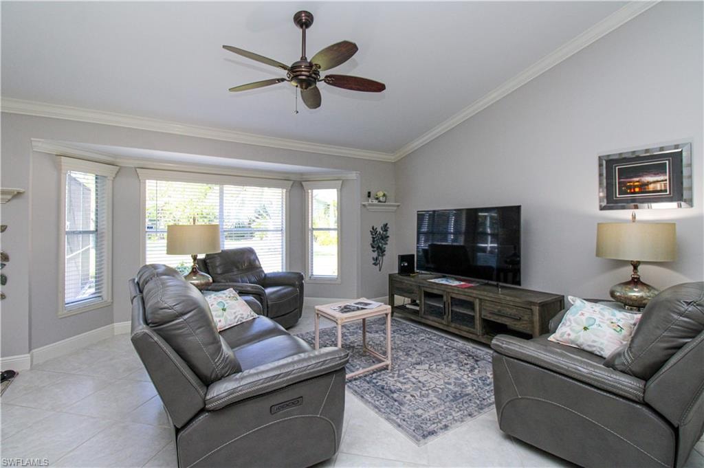 Living area featuring vaulted ceiling, light tile patterned floors, a ceiling fan, and ornamental molding