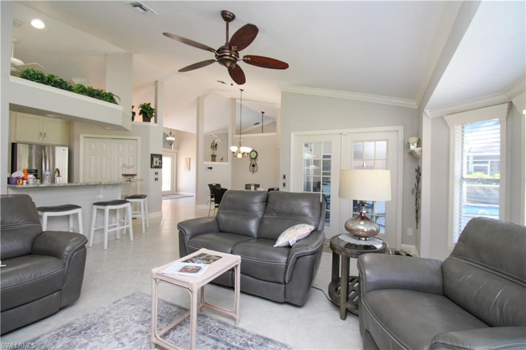 Living room with visible vents, lofted ceiling, ornamental molding, light tile patterned floors, and a ceiling fan
