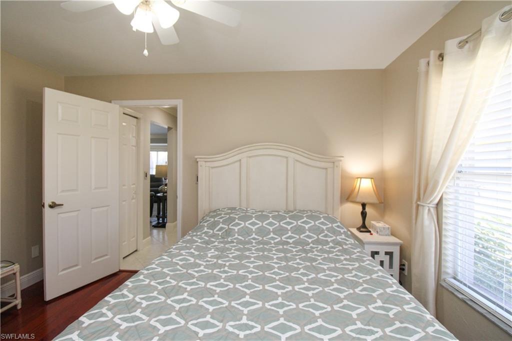 Bedroom featuring ceiling fan, baseboards, multiple windows, and dark wood-style floors