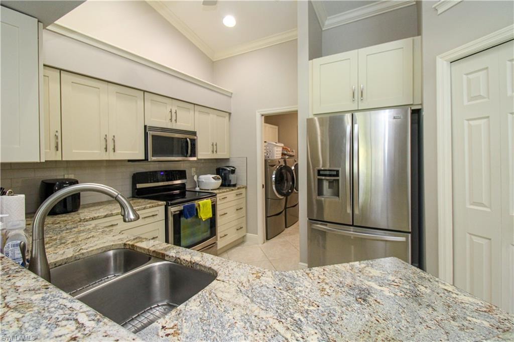 Kitchen featuring light tile patterned flooring, a sink, appliances with stainless steel finishes, washing machine and dryer, and tasteful backsplash