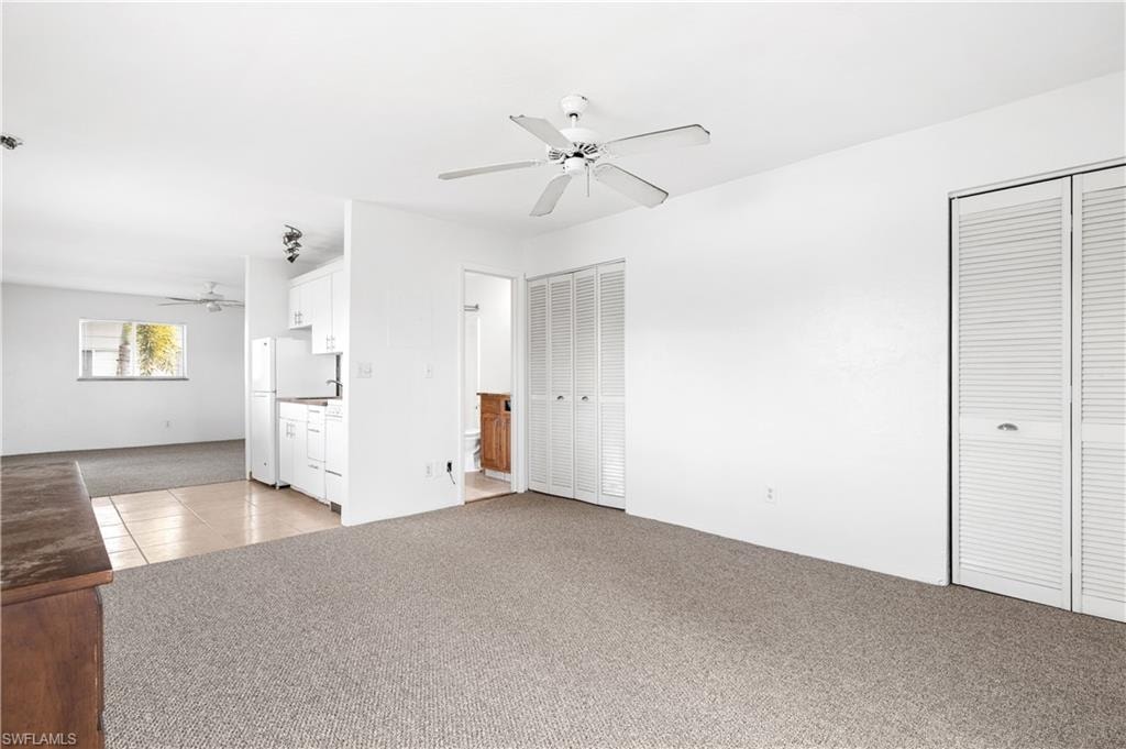 Unfurnished bedroom with light carpet, two closets, light tile patterned floors, and ceiling fan