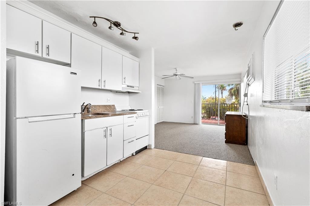 Kitchen with white appliances, white cabinetry, light colored carpet, dark countertops, and ceiling fan
