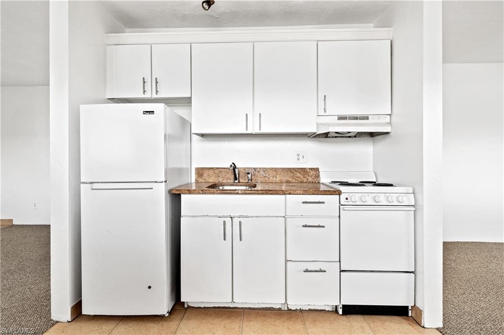 Kitchen with white appliances, white cabinetry, light carpet, and light tile patterned flooring