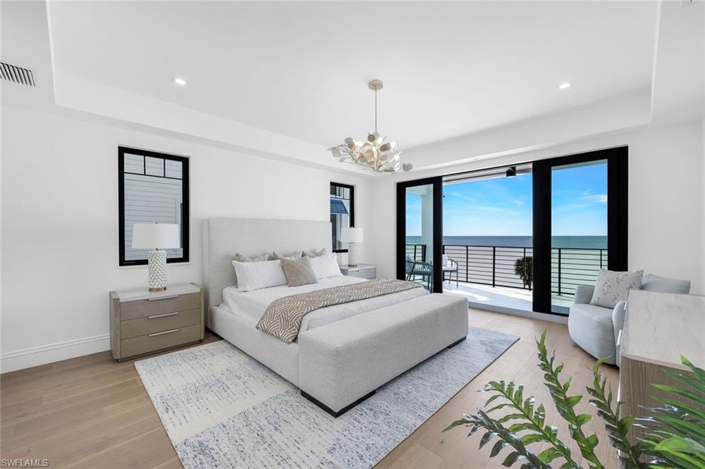 Bedroom with a water view, a raised ceiling, light wood-style flooring, access to exterior, and suspended lighting
