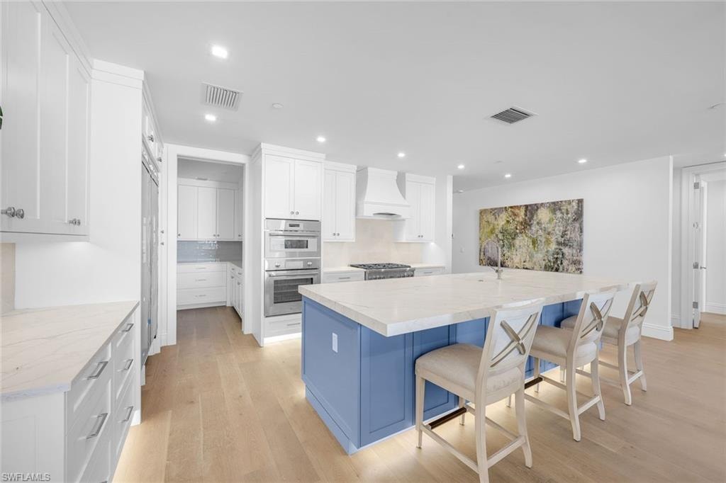Kitchen with a large island, dual tone cabinets, light wood finished floors, double oven, and recessed lighting
