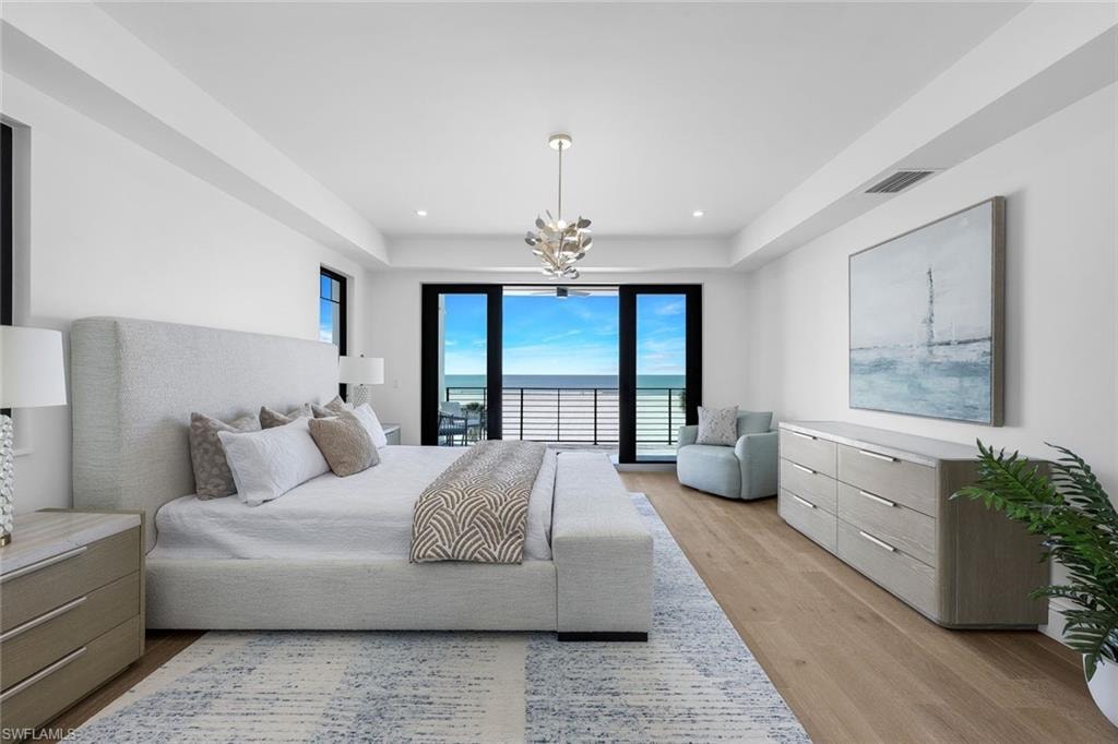 Bedroom featuring hanging lights, access to exterior, multiple windows, light wood-type flooring, and a tray ceiling