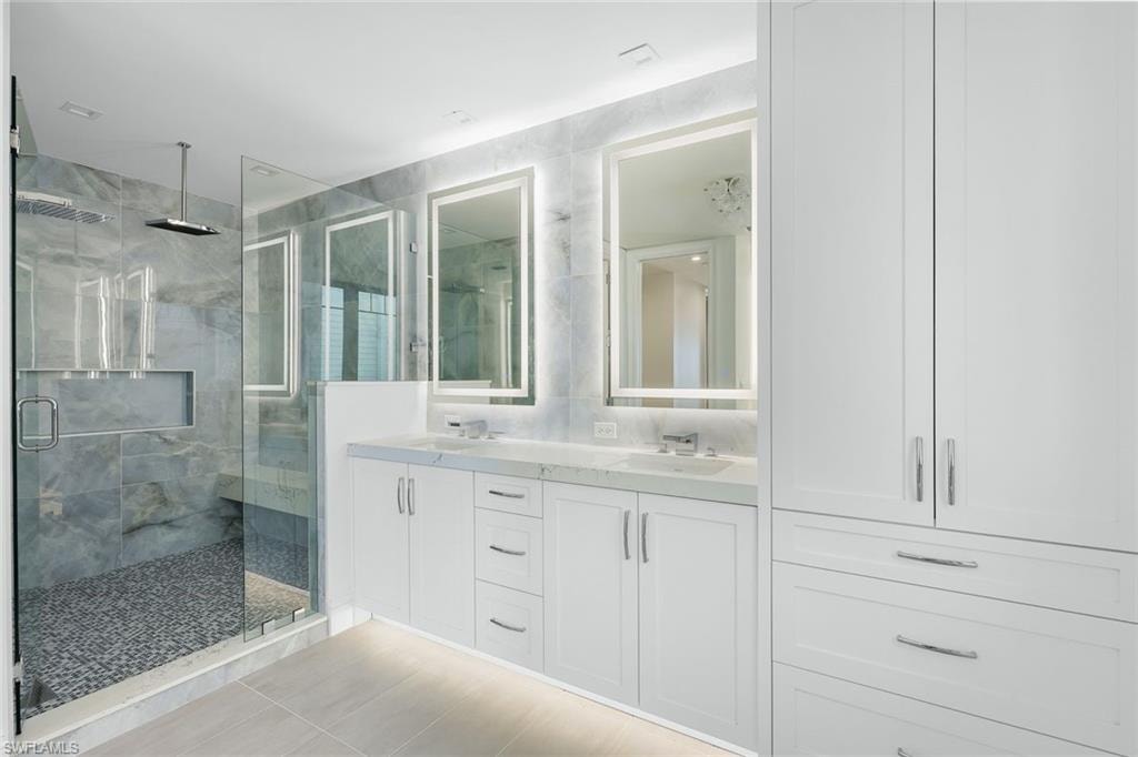 Full bathroom featuring double vanity, a marble finish shower, and light tile patterned floors