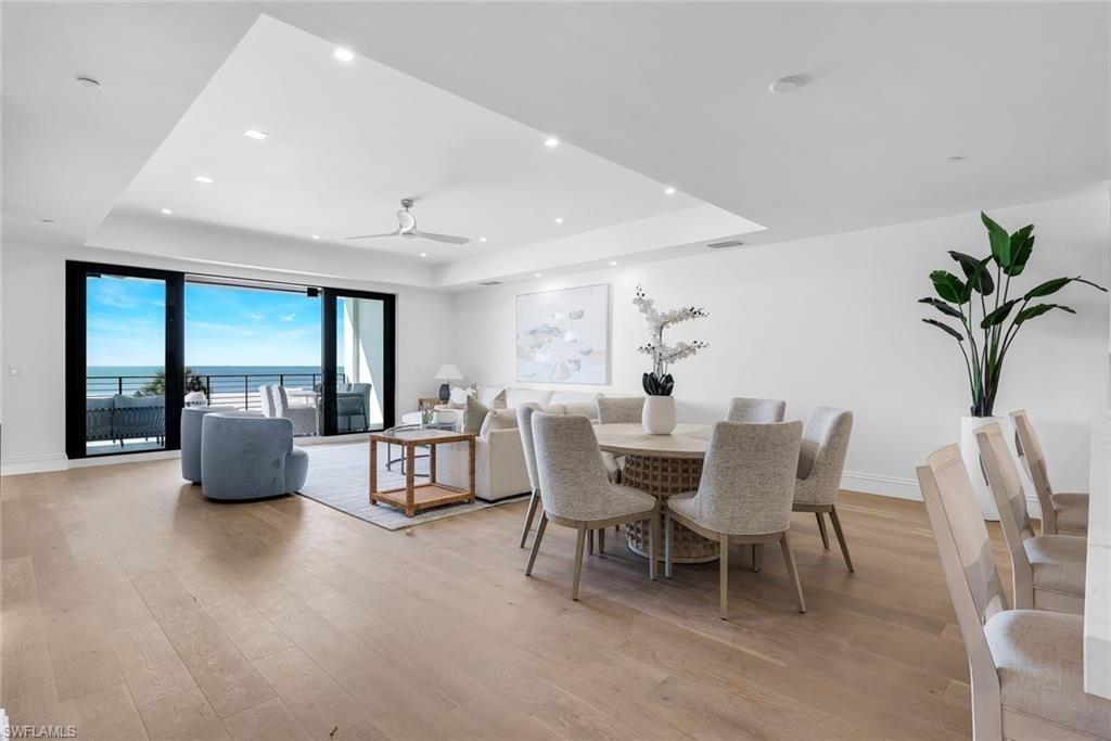 Dining area with a water view, a tray ceiling, a ceiling fan, light wood finished floors, and recessed lighting