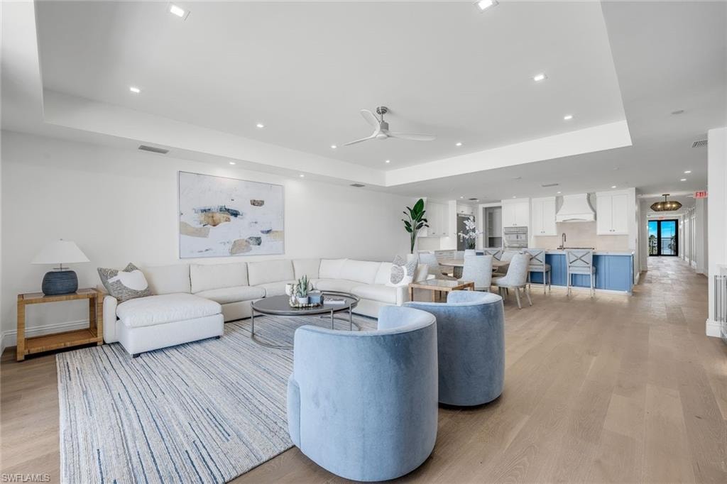 Living room with a ceiling fan, light wood-style flooring, a tray ceiling, and recessed lighting