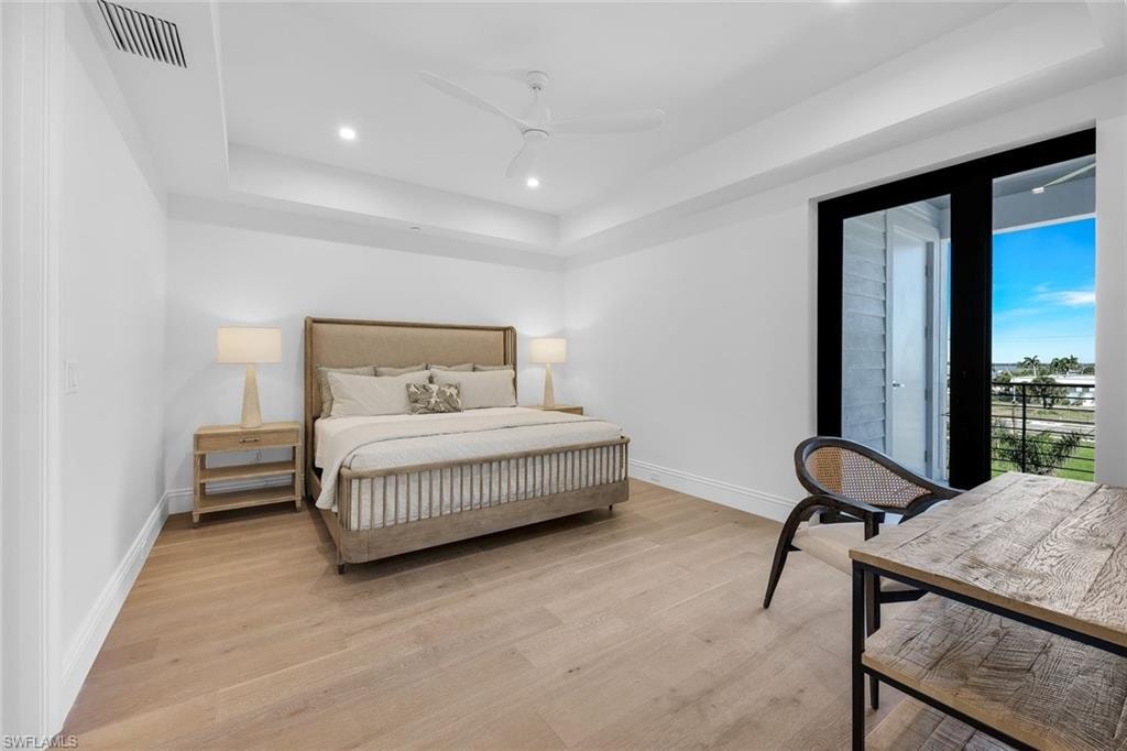 Bedroom featuring access to outside, a tray ceiling, light wood-type flooring, recessed lighting, and a ceiling fan