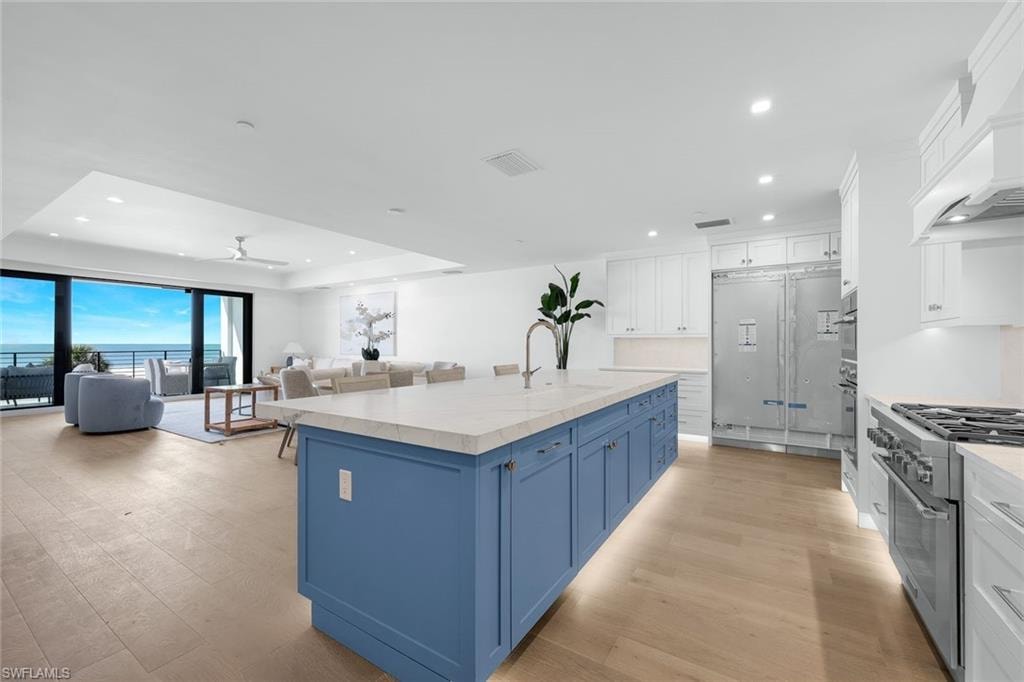 Kitchen featuring two tone color scheme, high end stove, a center island with sink, open floor plan, and recessed lighting