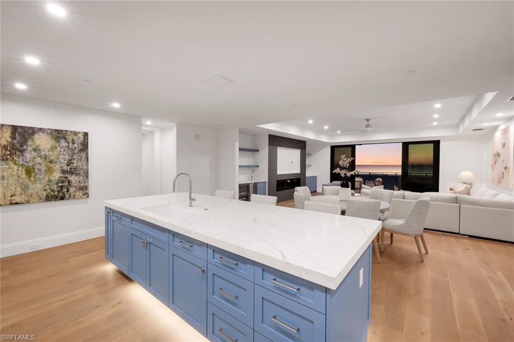 Kitchen featuring blue cabinetry, a ceiling fan, an island with sink, light wood-type flooring, and open floor plan