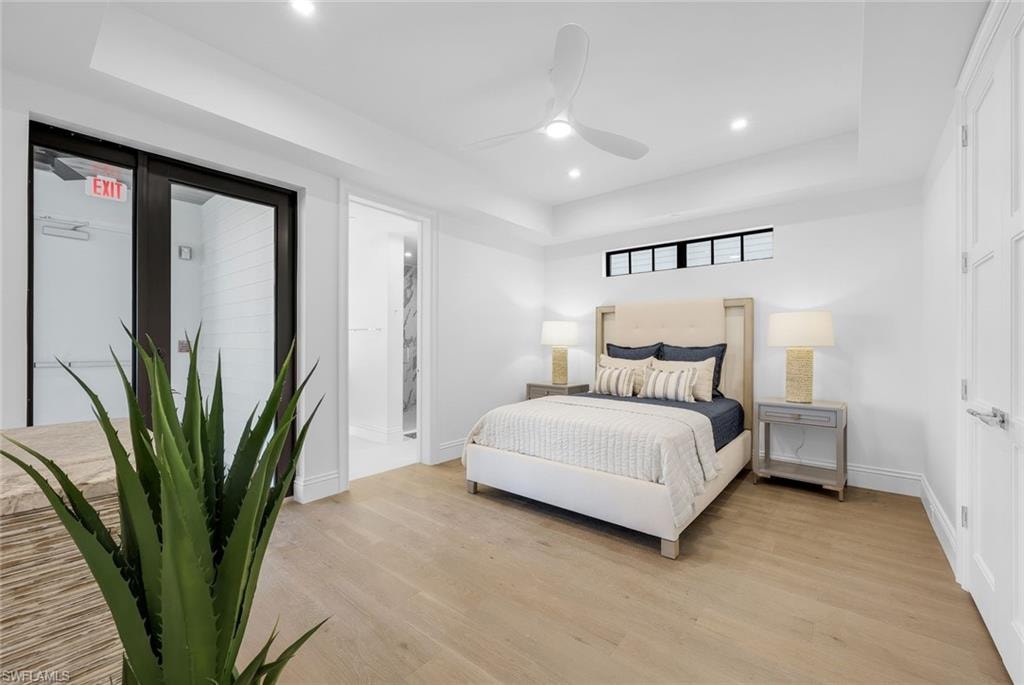 Bedroom with recessed lighting, a tray ceiling, light wood finished floors, a ceiling fan, and ensuite bathroom