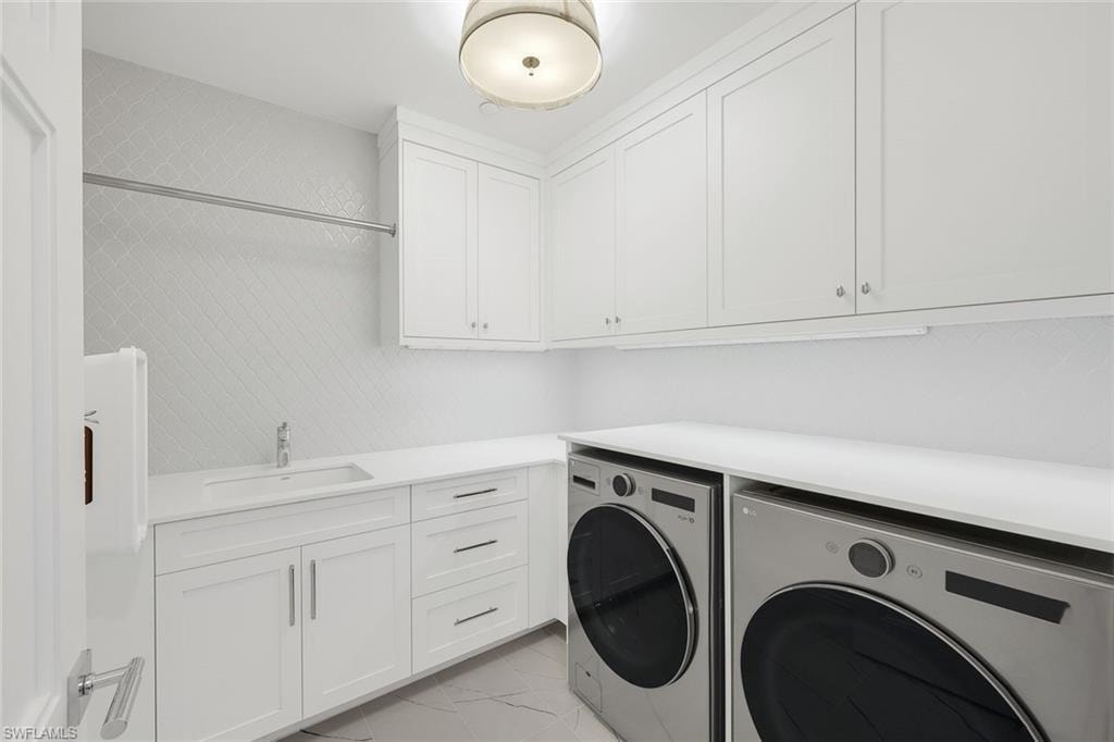 Laundry area featuring washing machine and dryer, cabinet space, and light marble finish floors