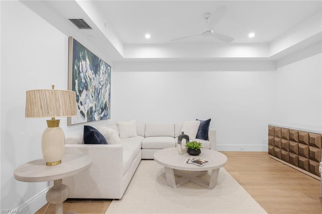 Living room featuring light wood finished floors, a ceiling fan, a tray ceiling, and recessed lighting