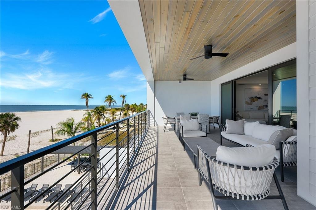 Balcony featuring view of water and beach, a ceiling fan, and outdoor seating