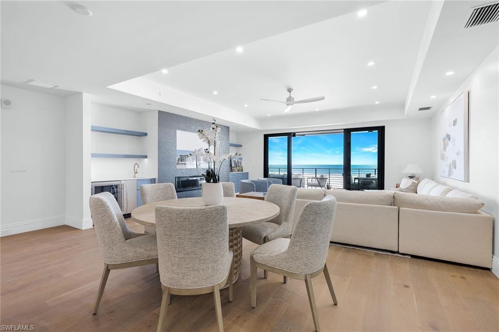 Dining space featuring light wood-type flooring, ceiling fan, a raised ceiling, wet bar, and wine cooler