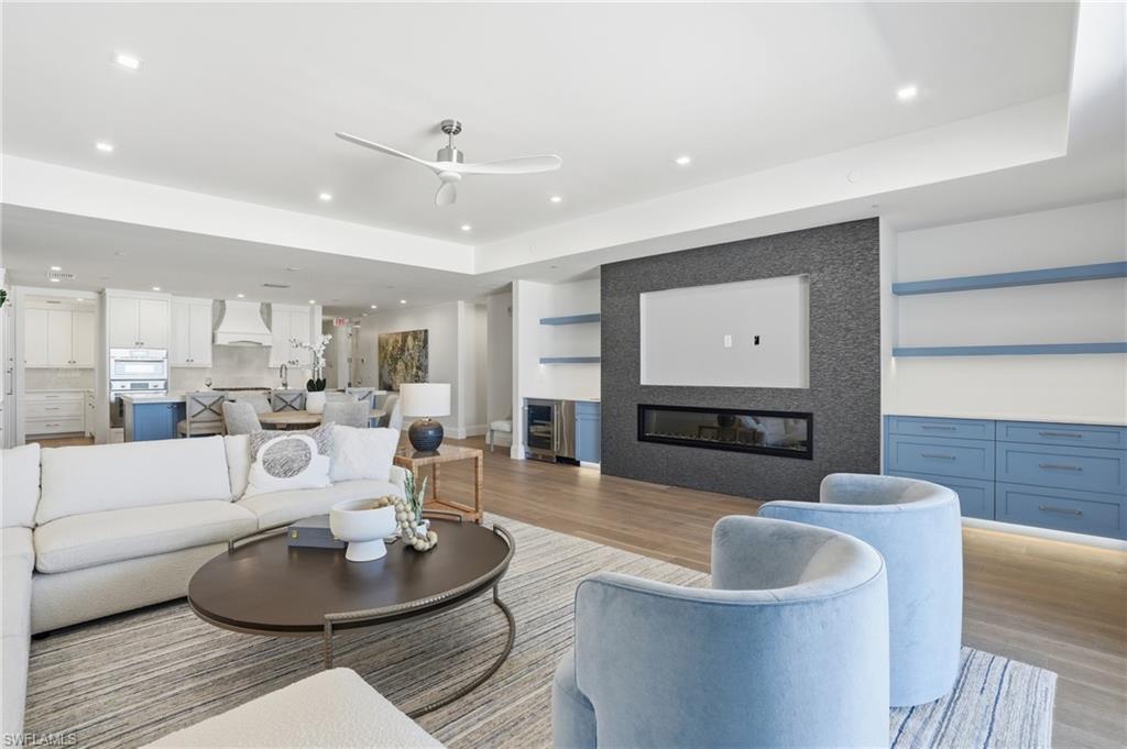 Living area with a large fireplace, ceiling fan, wood finished floors, beverage cooler, and recessed lighting