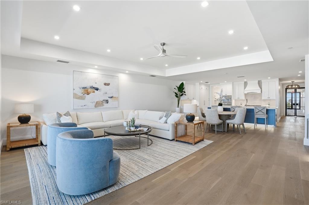 Living room featuring a tray ceiling, light wood-style flooring, a ceiling fan, and recessed lighting