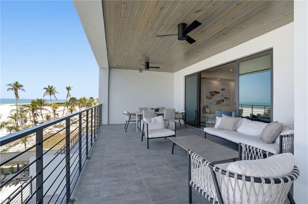 Balcony with view of water and beach, a ceiling fan, and an outdoor hangout area