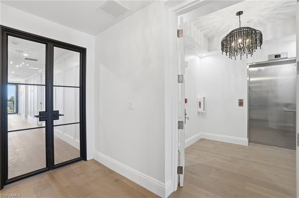 Corridor with elevator, light wood finished floors, a chandelier, and french doors