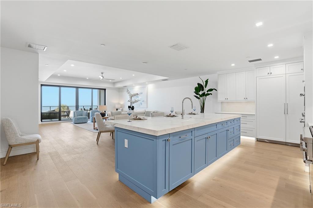Kitchen featuring an island with sink, two tone cabinetry, open floor plan, a ceiling fan, and a tray ceiling