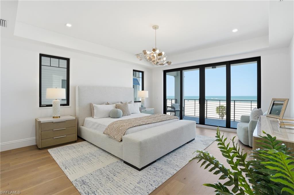 Bedroom with a water view, a tray ceiling, access to exterior, light wood-style floors, and suspended lighting