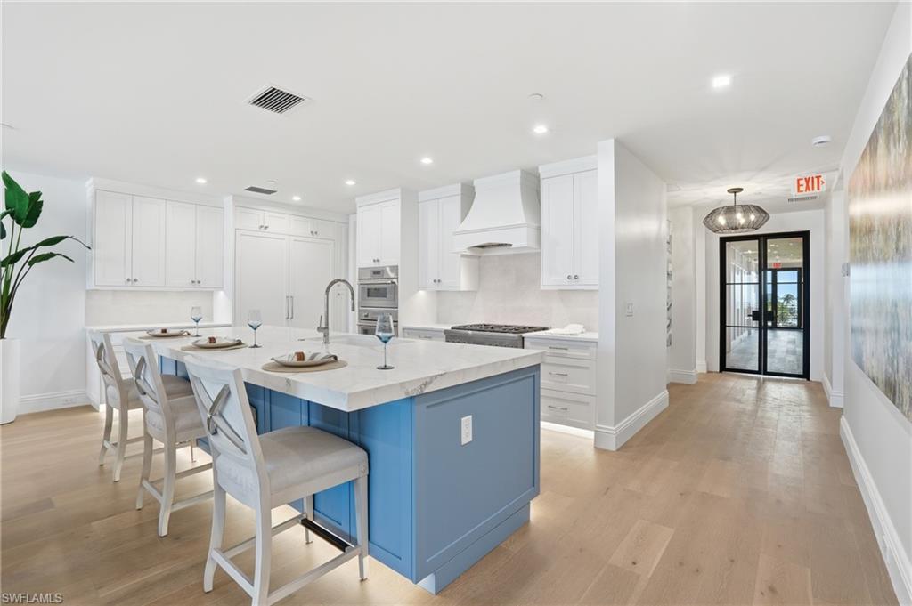 Kitchen with a kitchen bar, two tone cabinets, a kitchen island with sink, light wood-type flooring, and light stone counters