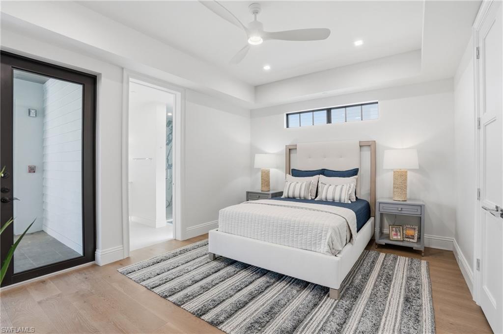 Bedroom featuring recessed lighting, ceiling fan, a tray ceiling, light wood finished floors, and connected bathroom