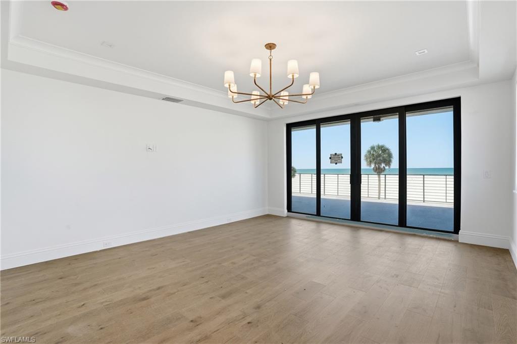 Unfurnished room with a raised ceiling, suspended lighting, light wood-type flooring, and a water view
