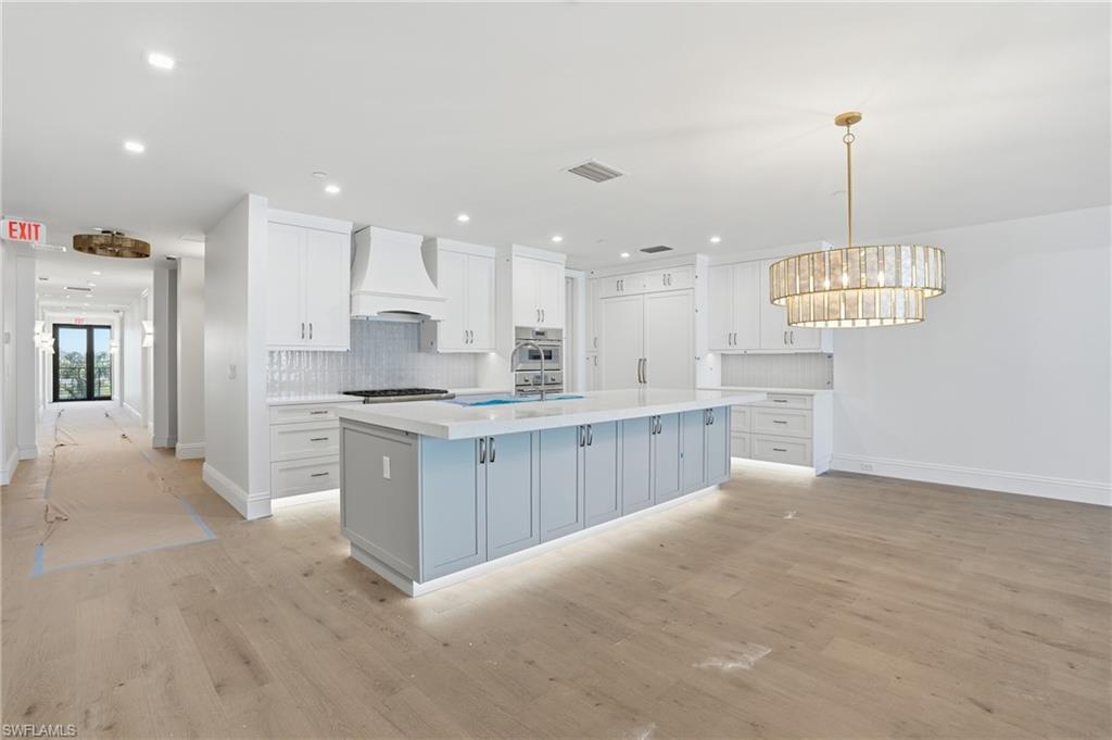 Kitchen featuring light wood-style floors, an island with sink, decorative backsplash, stainless steel oven, and dual tone cabinetry