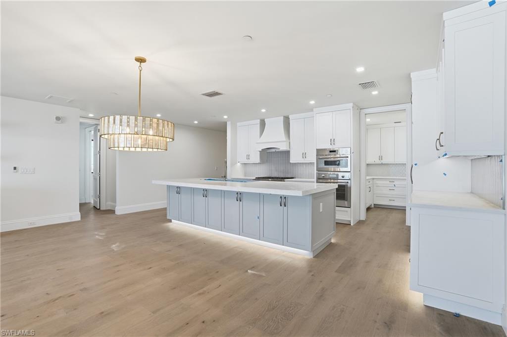 Kitchen with backsplash, a center island with sink, light wood-style flooring, white cabinets, and stainless steel double oven