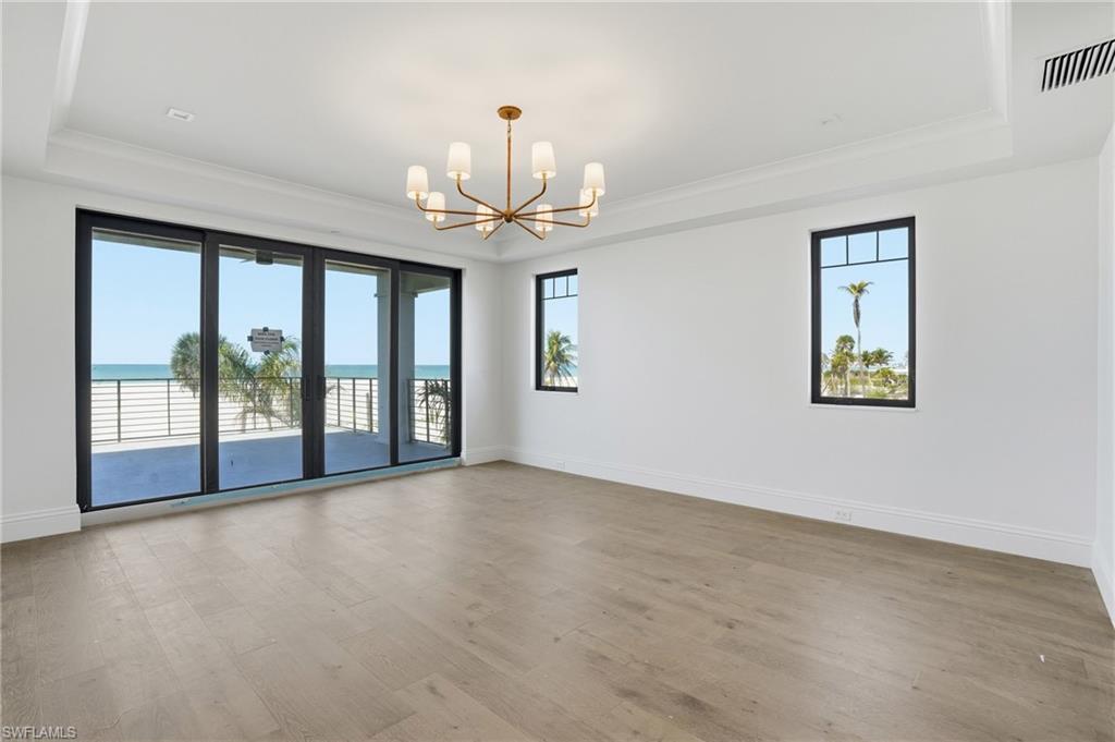 Empty room featuring a raised ceiling, suspended lighting, plenty of natural light, light wood-style flooring, and a water view