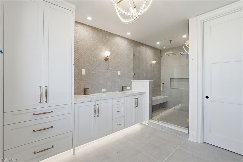 Full bath featuring double vanity, a stall shower, suspended lighting, tile walls, and light tile patterned floors