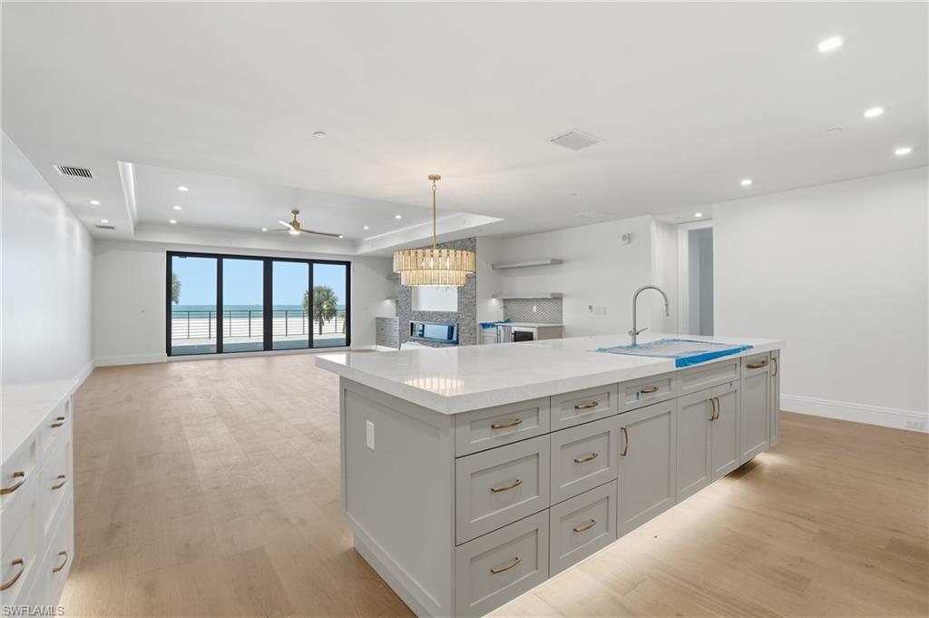 Kitchen featuring a tray ceiling, a kitchen island with sink, light wood-type flooring, open floor plan, and ceiling fan