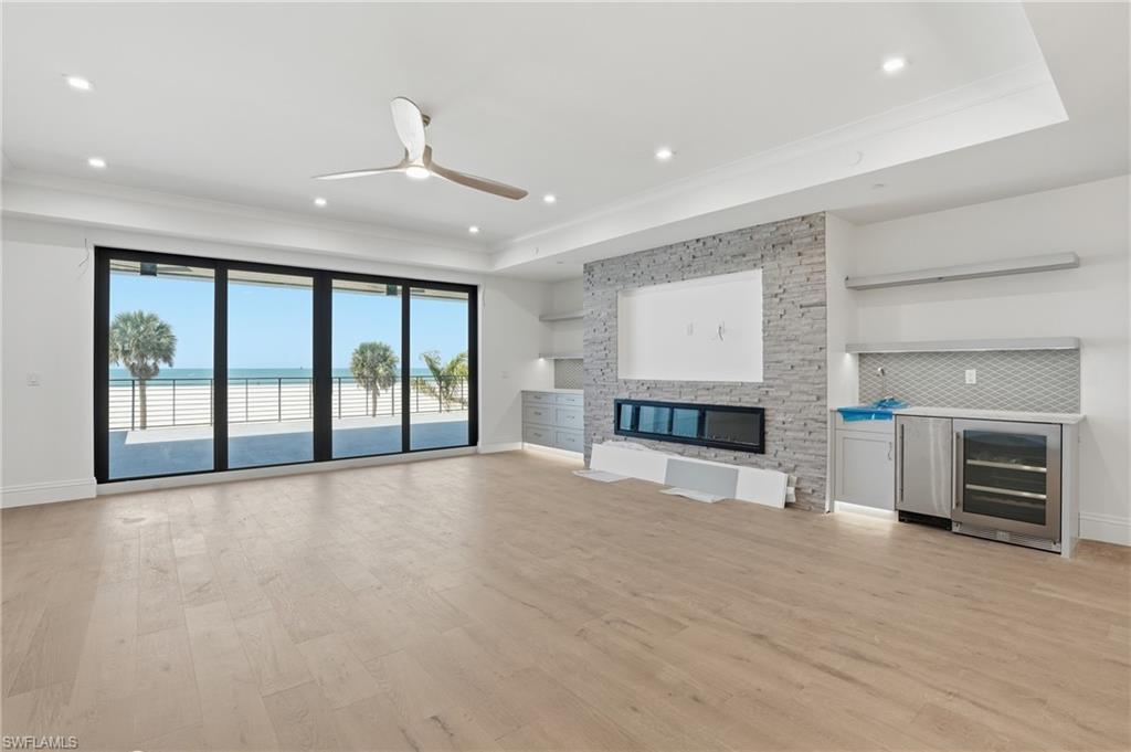 Unfurnished living room with ceiling fan, wine cooler, light wood-style flooring, ornamental molding, and a water view