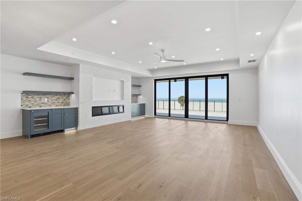 Unfurnished living room featuring a premium fireplace, a raised ceiling, light wood-style floors, a ceiling fan, and recessed lighting