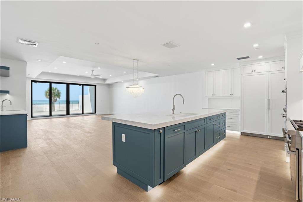 Kitchen with open floor plan, dual tone cabinetry, high end range, an island with sink, and light wood-style floors