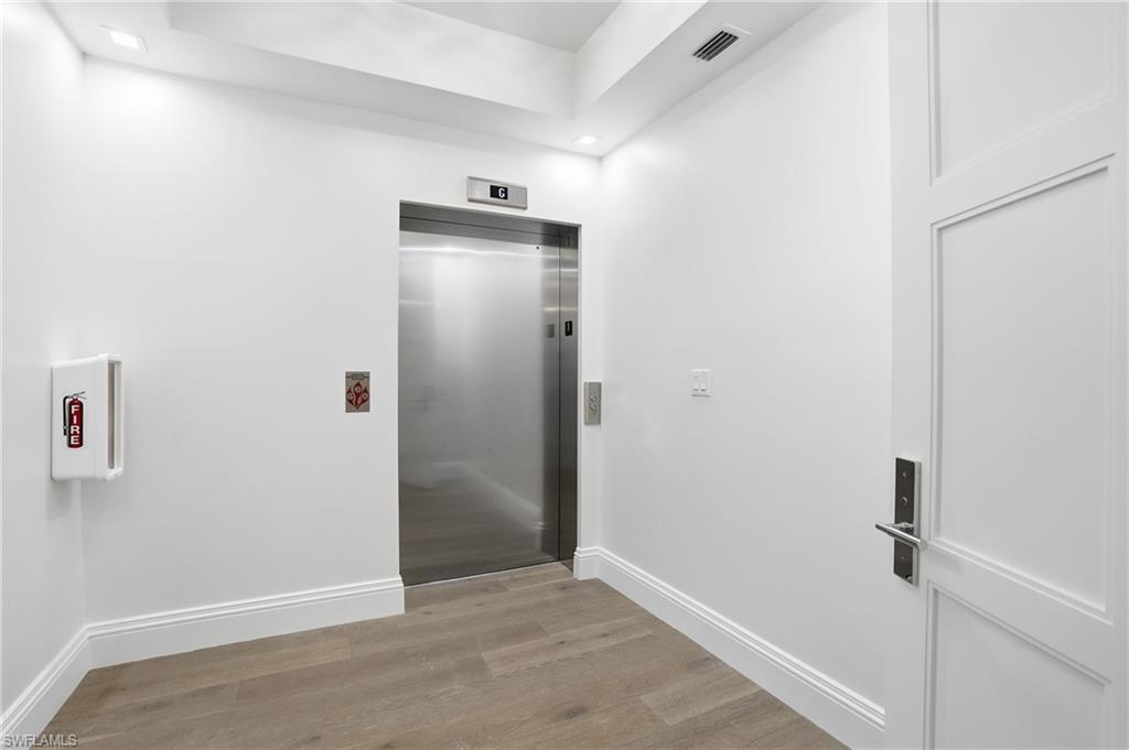 Hallway featuring light wood-type flooring, elevator, and recessed lighting