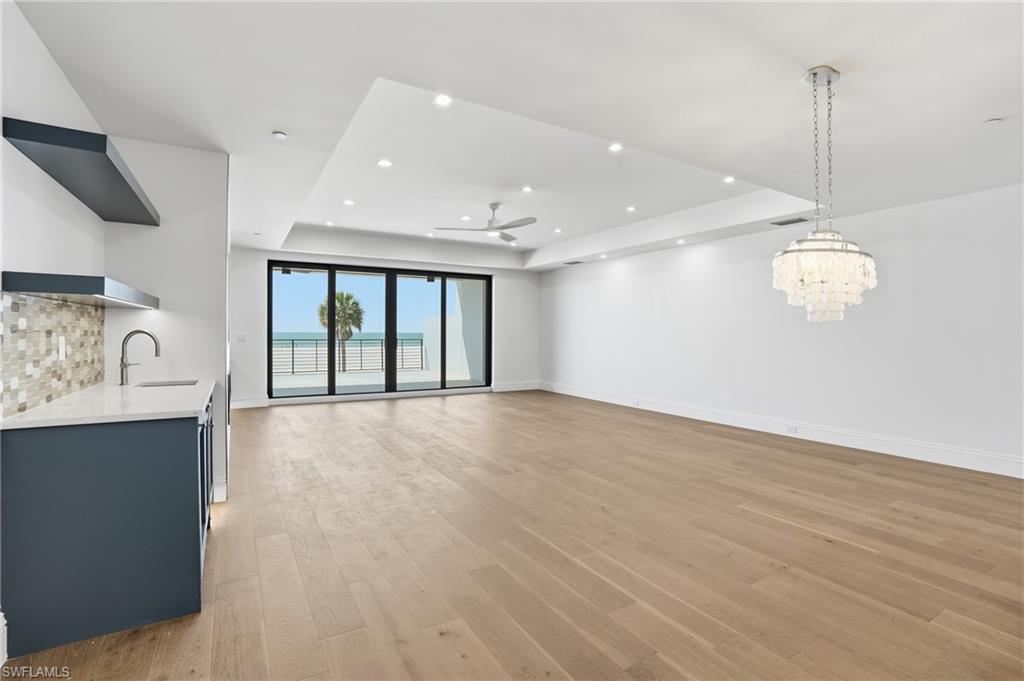 Unfurnished living room featuring light wood-type flooring, a ceiling fan, a raised ceiling, and suspended lighting