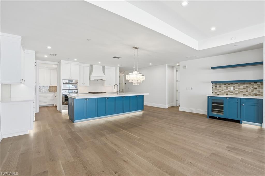 Dual tone kitchen featuring backsplash, an island with sink, light wood-type flooring, stainless steel double oven, and dual tone cabinets
