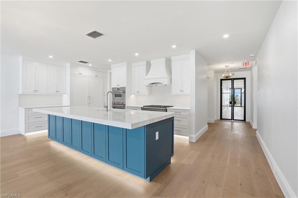 Two tone kitchen with dual tone cabinets, an island with sink, light wood-style flooring, light stone countertops, and recessed lighting