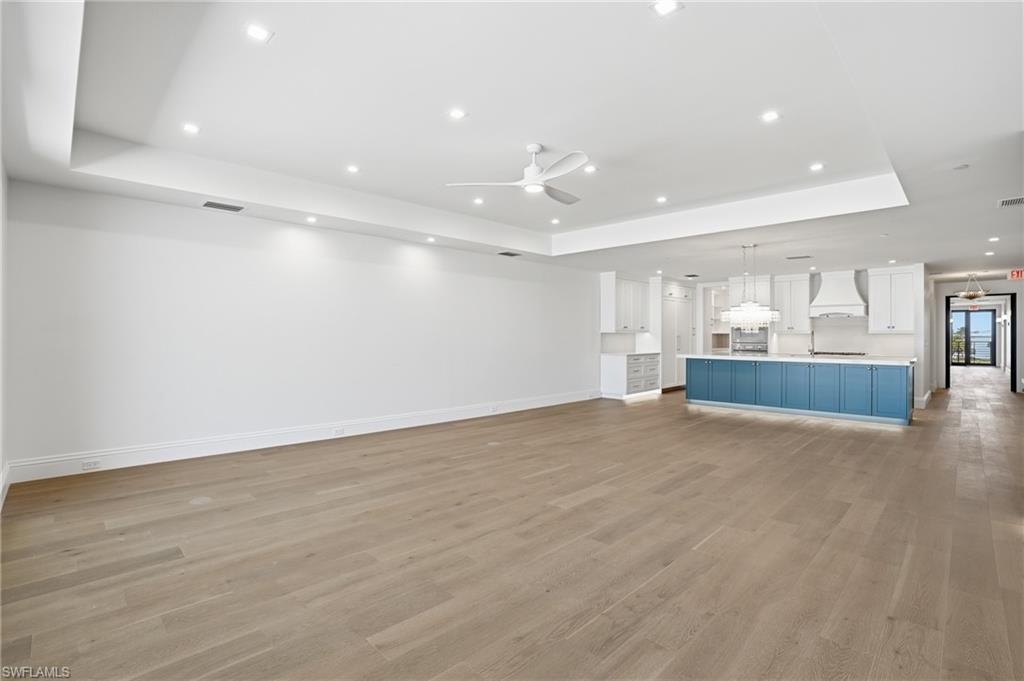 Unfurnished living room with a tray ceiling, a ceiling fan, light wood-type flooring, and recessed lighting