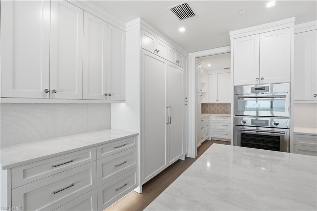 Kitchen with white cabinetry, double oven, light stone countertops, decorative backsplash, and recessed lighting
