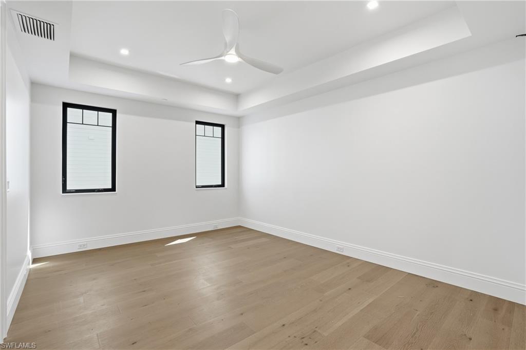 Empty room featuring a raised ceiling, ceiling fan, light wood finished floors, and recessed lighting