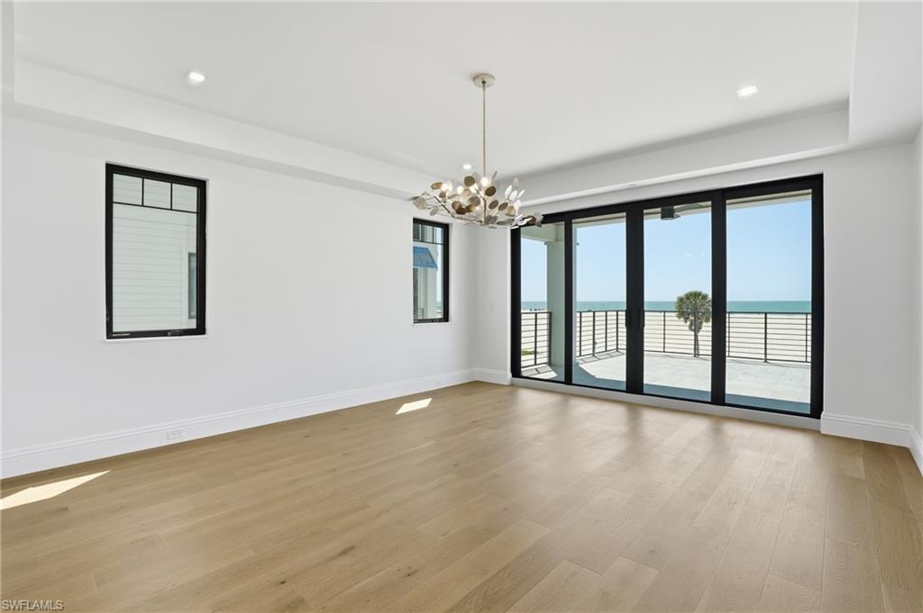 Empty room with a raised ceiling, a water view, hanging lights, and light wood-style flooring