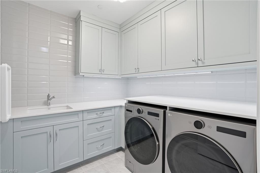 Laundry area featuring washer and clothes dryer, light tile patterned floors, cabinet space, and tile walls