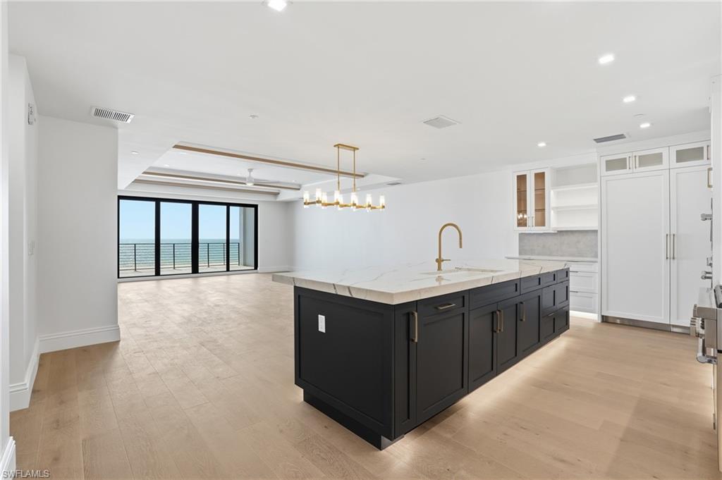Dual tone kitchen featuring glass fronted cabinets, dual tone cabinets, an island with sink, light stone counters, and open floor plan